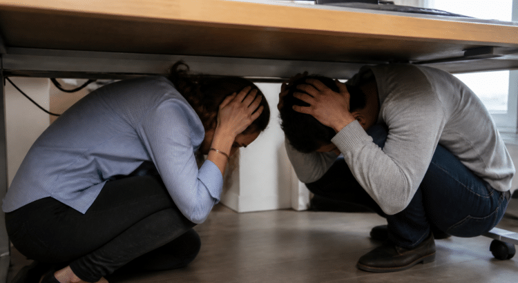 Personnes accroupies sous bureau pendant tremblement terre